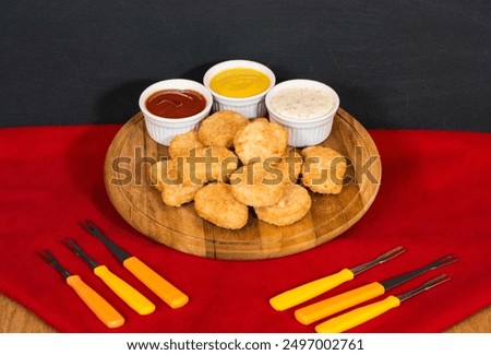 Top view of appetizers table with chicken nuggets, mayonnaise, ketchup and mustard. Food board with beer and cutlery next to it.