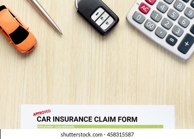 Top view of approved car insurance claim form with key and calculator on wooden desk.