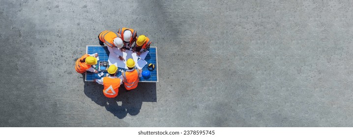 Top view of architect engineer working on solar panel and his blueprints with solar photovoltaic equipment and wind turbine on construction site. clean energy concept. copy space for text and design.