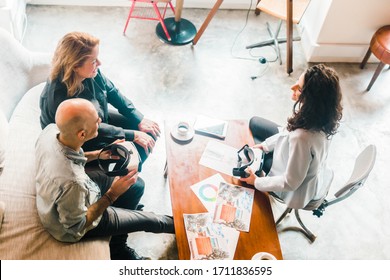 Top View Of Architect Talking With Clients In Office. Cheerful Mature Couple Discussing Design Of New Home And Holding VR Glasses. New House Project, Renovation Concept