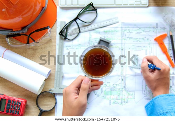 Top View Architect working on blueprint.\
Architects workplace.  Engineer tools and safety control, \
blueprints, ruler, orange helmet,radio,laptop and divider compass.\
Construction Concept.