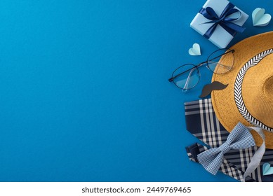 Top view arrangement for Fathers' Day featuring straw hat, necktie, bow tie, giftbox, glasses, mustache props, and hearts on blue surface. Space reserved for personalized greetings or promotional text