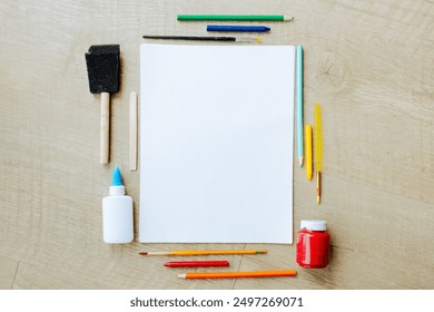 A top view of art supplies neatly arranged around a blank sheet of paper. Items include colored pencils, a paintbrush, glue bottle, and a jar of paint, ready for a creative project or education - Powered by Shutterstock