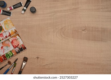 Top view of art supplies with watercolor paint, palette and paintbrushes on wooden surface for a painting session - Powered by Shutterstock