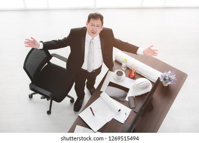 Top View Of Asian Business Man In Black Suit, Wearing Glasses, Standing Between Table And Chair, Look Upwards, Arms Wide Open With Drawing, White Safety Helmet, Tablet, Smartphone, Office Background