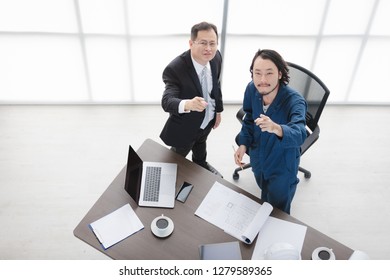 Top View Of Asian Business Man And Male Foreman In Coverall, Happily Look Up At Camera, Satisfy With New Project, On Laptop, Smartphone, Smart Office Background