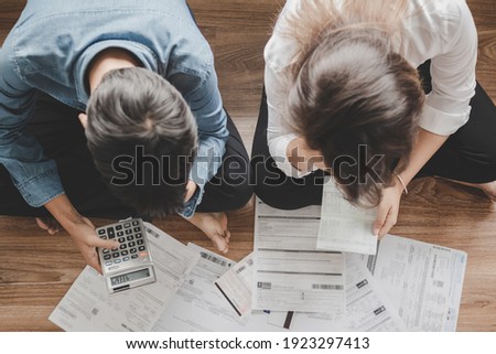 Top view asian couple sitting on the floor stressed and confused by calculate expense from invoice or bill, have no money to pay think of taking the house to mortgage causing debt, bankruptcy concept.