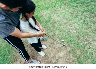 Top View Of Asian Father And Giving Young Daughter Golf Lesson.