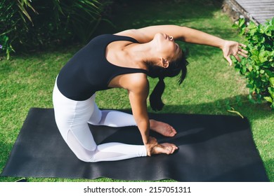 Top View Of Asian Girl Practicing Yoga In Camel Pose Outdoor. Healthy Lifestyle. Young Focused Woman With Closed Eyes Wearing Sportswear And Barefoot On Fitness Mat On Green Grass In Yard. Bali Island