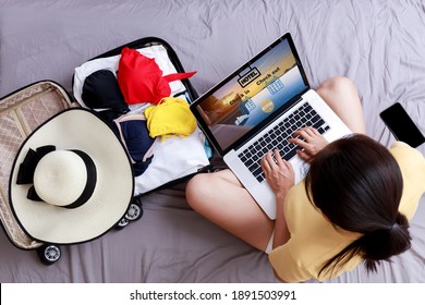 Top View Asian Happy Woman Plan For Trip By Laptop Booking Hotel On The Bed At Home. Women With Travel Bag Use Notebook Computer Internet Booking Hotel. Holiday Summer Vacation Concept