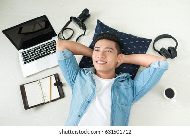 Top View Of Asian Man Lying On The Floor With Laptop, Camera, Tablet, Coffee And Phone