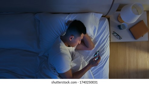 Top View Of Asian Man Use Smartphone To Watch Video On Bed At Night