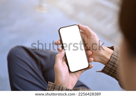 Top view of an Asian man using his smartphone while sitting at outdoor bench. mobile phone white screen mockup for display your graphic