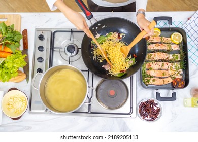 Top View Of Asian Woman Enjoy Cooking Healthy Food And Pasta In Cooking Pan On Stove In The Kitchen At Home. Happy Female Having Dinner Meeting Party Celebration With Friends On Holiday Vacation.