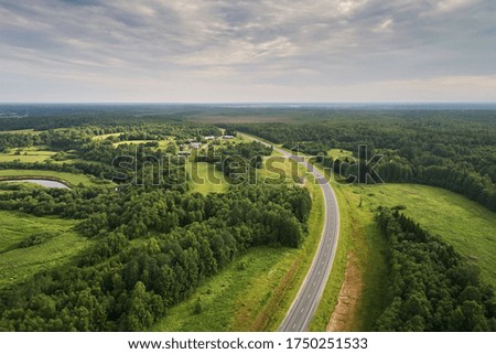 Top view of the asphalt road and dense green forests and sky. Beautiful bright landscape photography with drone on a summer day