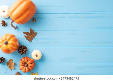 Top view of assorted autumn pumpkins, pinecones, and leaves on a blue wooden background. Ideal for seasonal and Thanksgiving themes