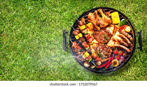 Top view of assorted delicious grilled meat with vegetables on barbecue grill with smoke and flames in green grass