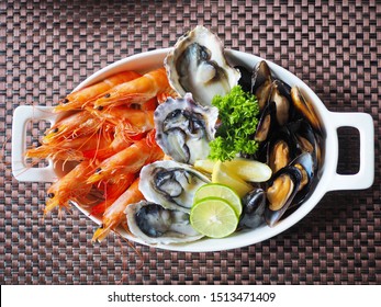 Top View Assorted Fresh Cooked Cold Seafood As Shrimps, Prawns, New Zealand Mussels, Mussels, Oyster, Rock Lobster, Lobster Claw With Yello Leomon In Oval Shaped Dish Or Plate On Ice On Wooden Table