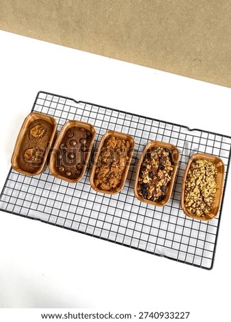 Top view of assorted homemade mini loaf cakes placed in paper baking molds and cooling on a metal wire rack over a white background.
