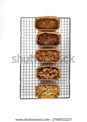 Top view of assorted homemade mini loaf cakes placed in paper baking molds and cooling on a metal wire rack over a white background.