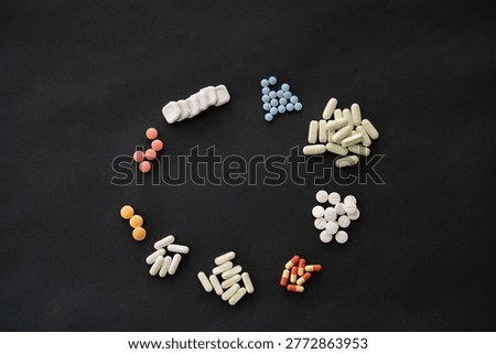 Top view of assorted pills and capsules arranged in organized groups on a dark background, representing medication types, dosage and healthcare concepts.