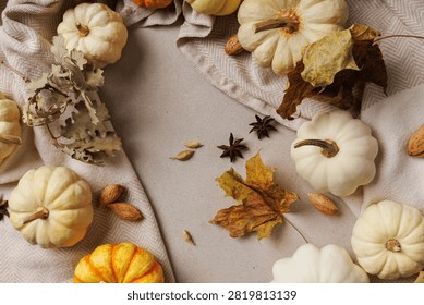 Top view of assorted pumpkins, almonds, dry leaves and spices on neutral fabric background..