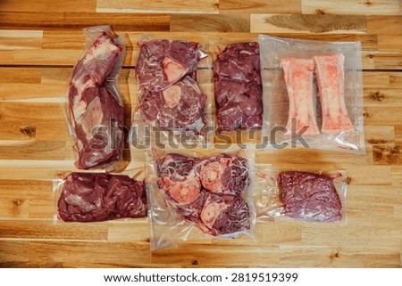 Top view of assorted raw beef cuts, organ meat, steaks, and marrow bones vacuum sealed in clear plastic bags on a wooden surface