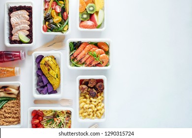 Top view of assorted ready meals over white background with copy space. Prawns, salmon with brown rice, asian noodles, pasta and meatballs, chicken and potato, mushrooms, vegetable and fruit salad. 