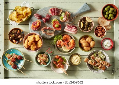 Top view of assorted snacks with kebabs or tapas placed near seafood and fried chicken served in bowls on table with assorted sausages