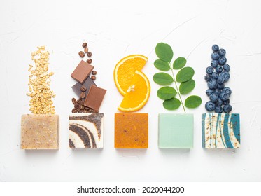 Top view of assorted variety of different handmade soap bars with natural ingredients, herbs, berries on white stone background. Skin care and organic soap making concept, spa cosmetic treatment 