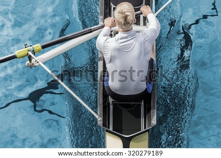 Top view of athletic competition rower, who strokes his  paddle through metallic blue water.