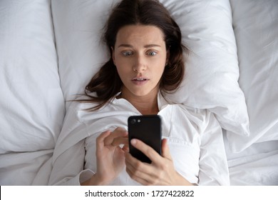 Top View Awakened Woman Lying In Bed Holds Smart Phone Looks At Screen Watching Time Overslept And Late Feels Stressed, Upset Female Read Received Awful News, Being Cheated Threaten Or Hacked Concept