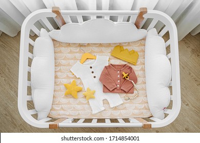 The top view of baby clothes and accessories in cot, cradle. Wooden cradle for newborn with white pillows in baby's room.  