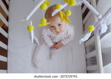 Top view of a baby sitting in crib and looking at hanging mobile. First skills, learning to sit.