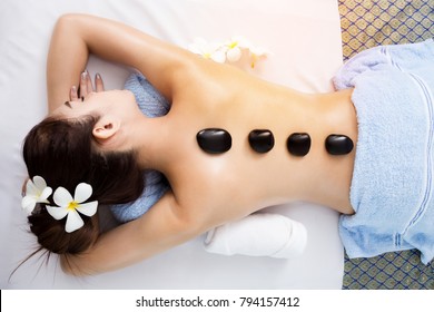 Top view of back of pretty asian woman lying on spa bed and have hot stone laying on her back, body and skin treatment in relaxation time, spa concept