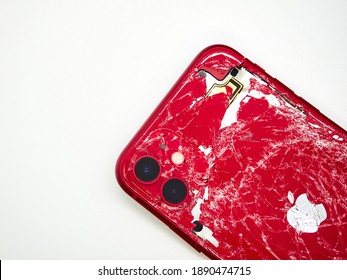Top view the back of red smartphone iPhone 11 with a broken glass and a damaged curved body close-up isolated on white background