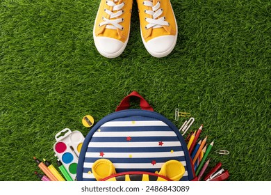 Top view of back to school supplies with backpack and yellow sneakers placed on green grass - Powered by Shutterstock