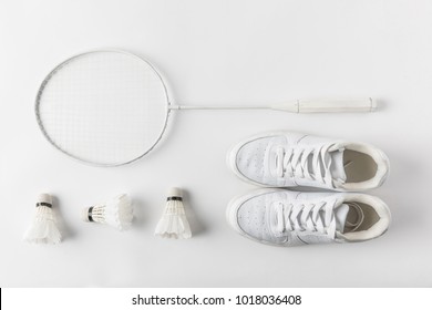 top view of badminton racket with suttercocks in row and sneakers on white surface
