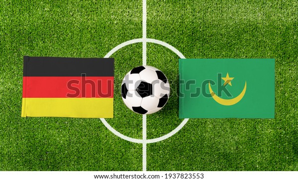 Top view ball with Germany vs. Mauritania flags\
match on green soccer\
field.