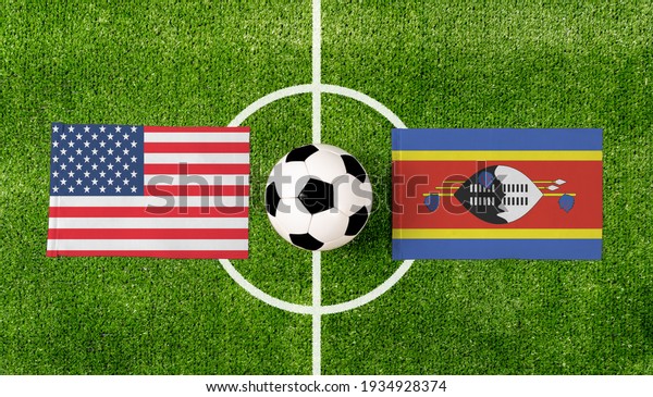 Top view ball with USA vs. Swaziland flags match\
on green soccer field.