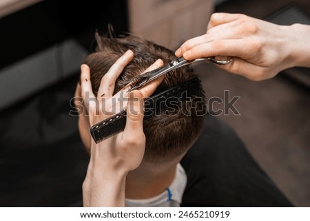 Top view barber uses scissors and comb to style the mans hair at the barbershop