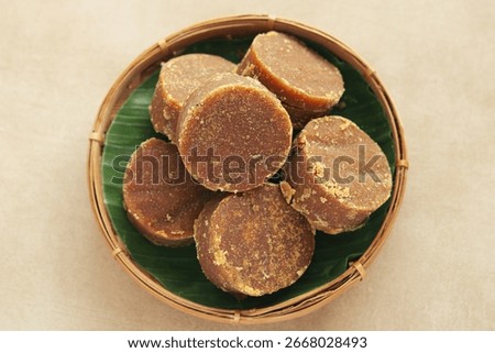Top view of a basket filled with solid, dark brown palm sugar discs (gula jawa or gula merah), a traditional sweetener used in a variety of desserts, beverages, and savory dishes.