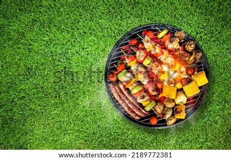 Top view of bbq grill, grilled meat, vegetables, mushrooms with flames and smoke. Placed on green grass lawn. Grilled food, copy space.