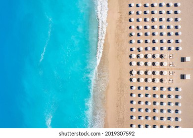 Top view of a beach with symmetrical sunbeds and parasols next to turquoise sea as seen in Greece