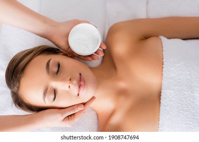 top view of beautician holding container with face mask near woman on massage table