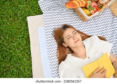 Top View, Beautiful And Attractive Young Asian Female Laying Down On Her Picnic Blanket With Her Favourite Book. Picnic Concept