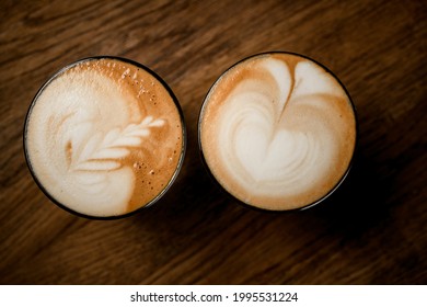 Top View Of Beautiful Glasses Of Hot Coffee With Art Pattern On White Foam On Wooden Table Background.