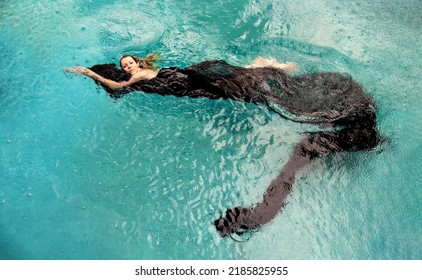 Top View To A Beautiful Sexy Young Woman Floating Like A Mermaid In Black Cloth Dress Wrapped In Green Water Of The Swimming Pool, Elegant Erotic Dream, Copy Space