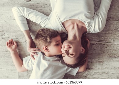 Top view of beautiful woman and her cute little son smiling while lying on the floor. Boy is kissing his mom in cheek
