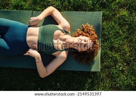 Top view of beautiful young happy sportive woman wearing green sports bra and blue yoga pant. Closed eyes and smiling while lying on yoga mat.